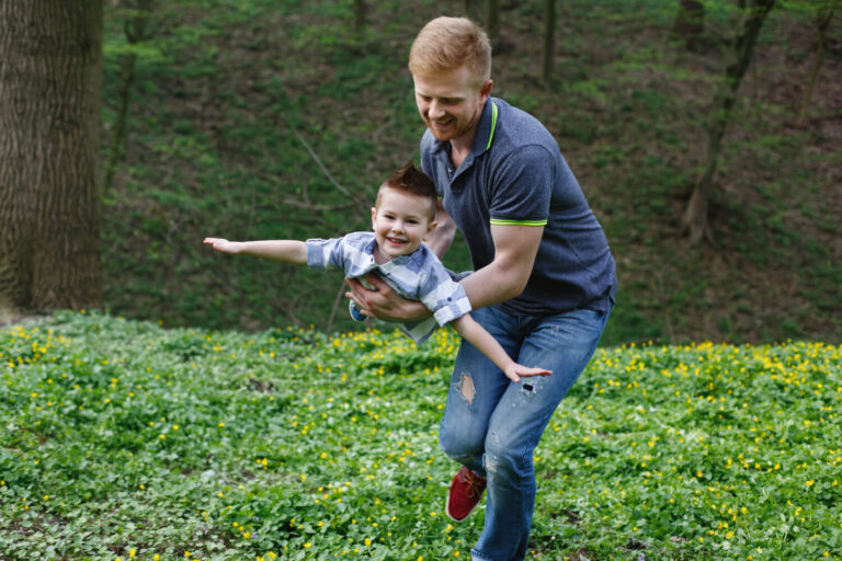 Pai brincando de aviãozinho com o filho em um parque florido, transmitindo segurança na Psicokids ABC.