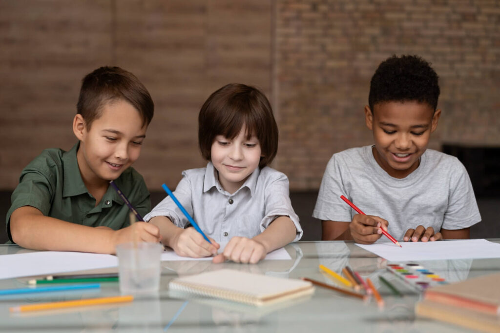 Três meninos sentados à mesa concentrados em desenhos e atividades escolares na Psicokids ABC.