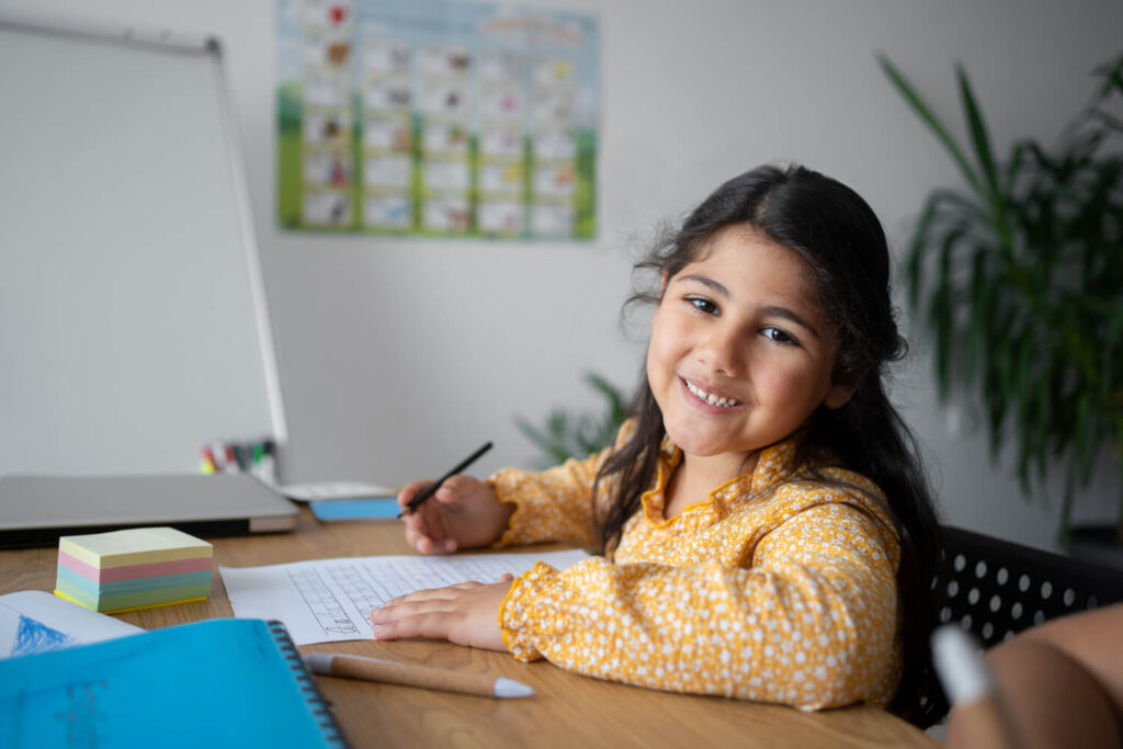 Menina sorridente com blusa amarela escreve em folha de atividades, estimulando a vontade de estudar na Clínica Psicokids no ABC.