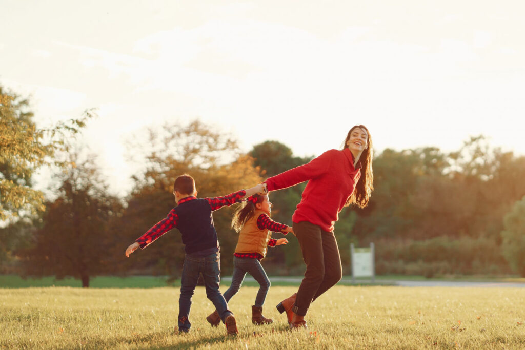 Mãe brinca com dois filhos pequenos em parque ensolarado. Apoio emocional na primeira infância pela Clínica Psicokids no ABC.