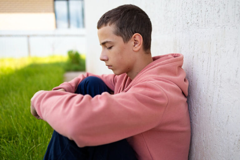 Adolescente de moletom rosa sentado triste com cabeça baixa, refletindo sinais de depressão na Clínica Psicokids, região do ABC.