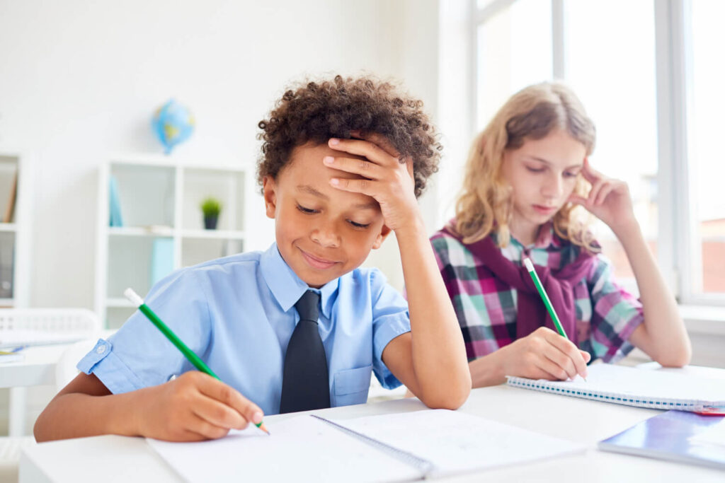 Menino de camisa azul com a mão na testa pensa diante de caderno. Entenda a dificuldade de interpretação de texto infantil na Psicokids ABC.