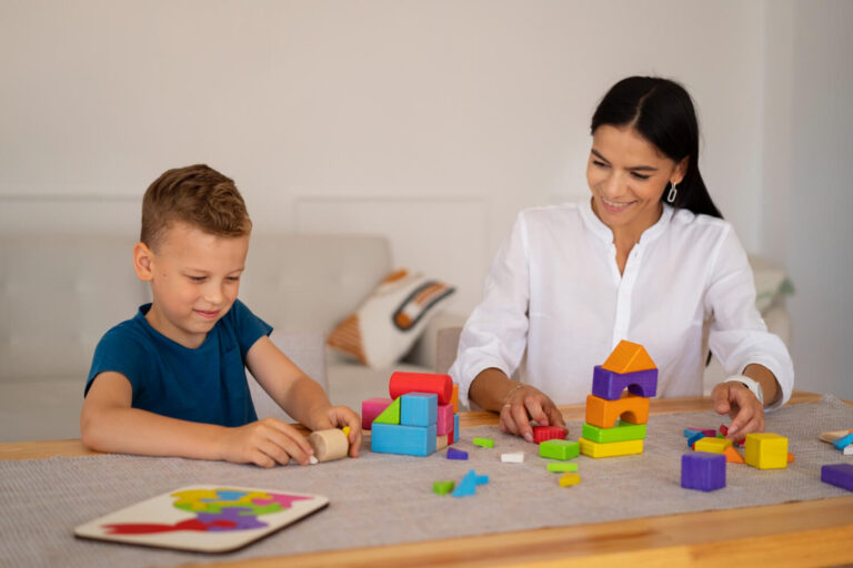 Psicopedagoga brincando com blocos educativos coloridos junto a um menino sorridente durante atendimento na Clínica Psicokids ABC.